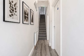 Un couloir avec un escalier, des tableaux encadrés accrochés au mur et une porte avec une pancarte.