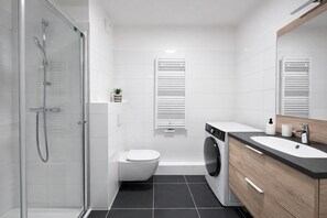 Ein modernes Badezimmer mit Duschkabine aus Glas, Toilette, Waschmaschine und Waschbecken mit Holzschrank.
