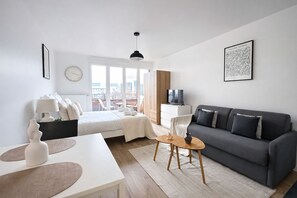 Ein modernes Wohnzimmer mit einem Bett, einem grauen Sofa, einem Fernseher und einem Essbereich mit Tisch und Stühlen.