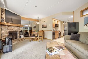 Ein Wohnzimmer mit Kamin, Essbereich und Küche mit Holzausstattung und Kühlschrank.