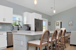 Een moderne keuken met witte kasten, een roestvrijstalen koelkast en een groot kookeiland met barstoelen.
