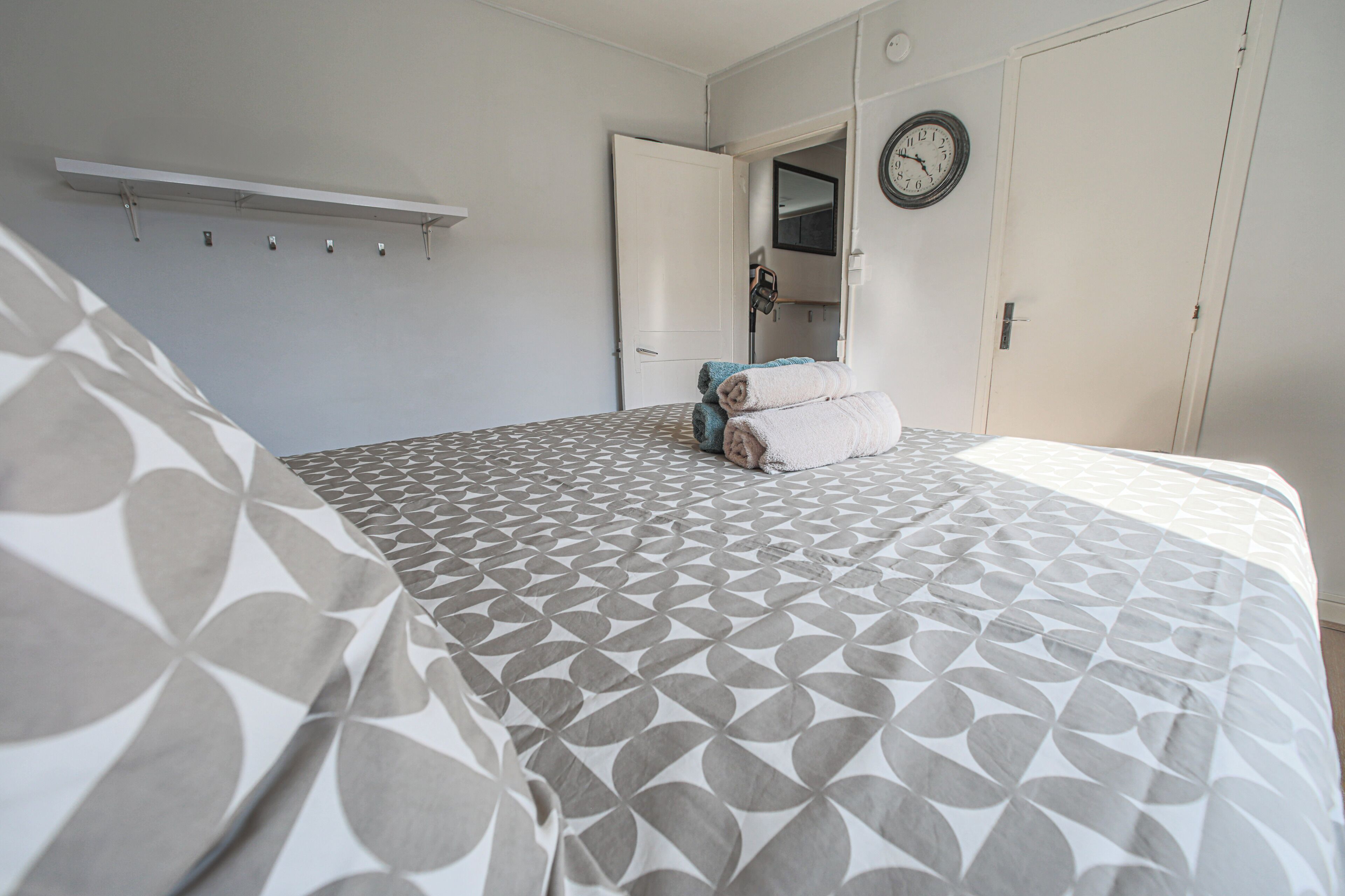 Une chambre à coucher avec une couvre-lit à motifs, une horloge murale et une porte donnant sur une salle de bain.