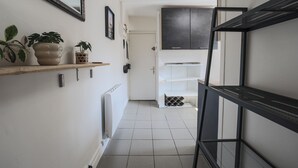 Un corridoio con termosifone, pianta in vaso, quadro appeso e una porta che dà su una stanza.