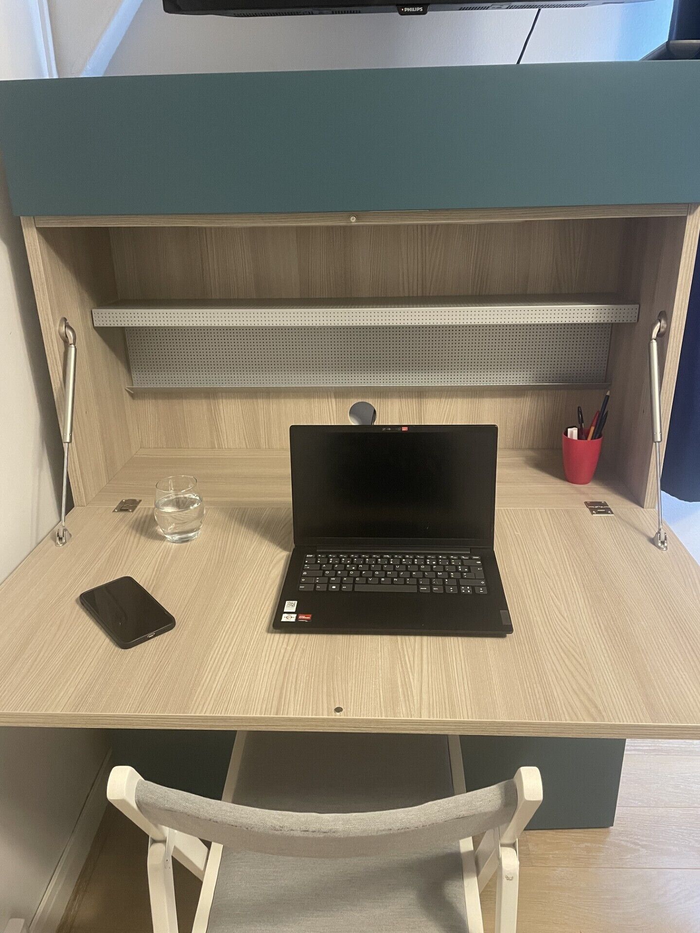 A wooden desk with a laptop, a smartphone, a glass of water, and a red cup.