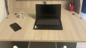 A wooden desk with a laptop, a smartphone, a glass of water, and a red cup.