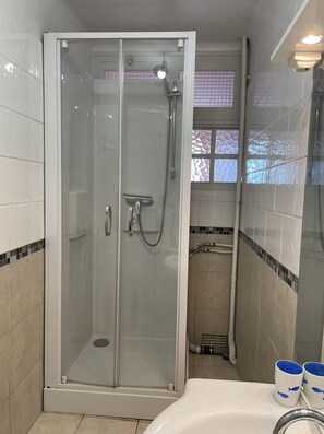 Une cabine de douche fermée par des parois en verre, équipée d’un pommeau de douche à main et d’un robinet à main.