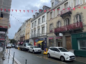 A street with buildings, a white car parked on the side, and a yellow truck. - A T3 apartment located in the city center, 5 minutes walk from the ST SERVAN beach. (Saint-Malo)