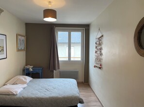 Une chambre à coucher avec un lit, un bureau, une fenêtre avec des rideaux, un élément de décoration suspendu et un miroir rond.