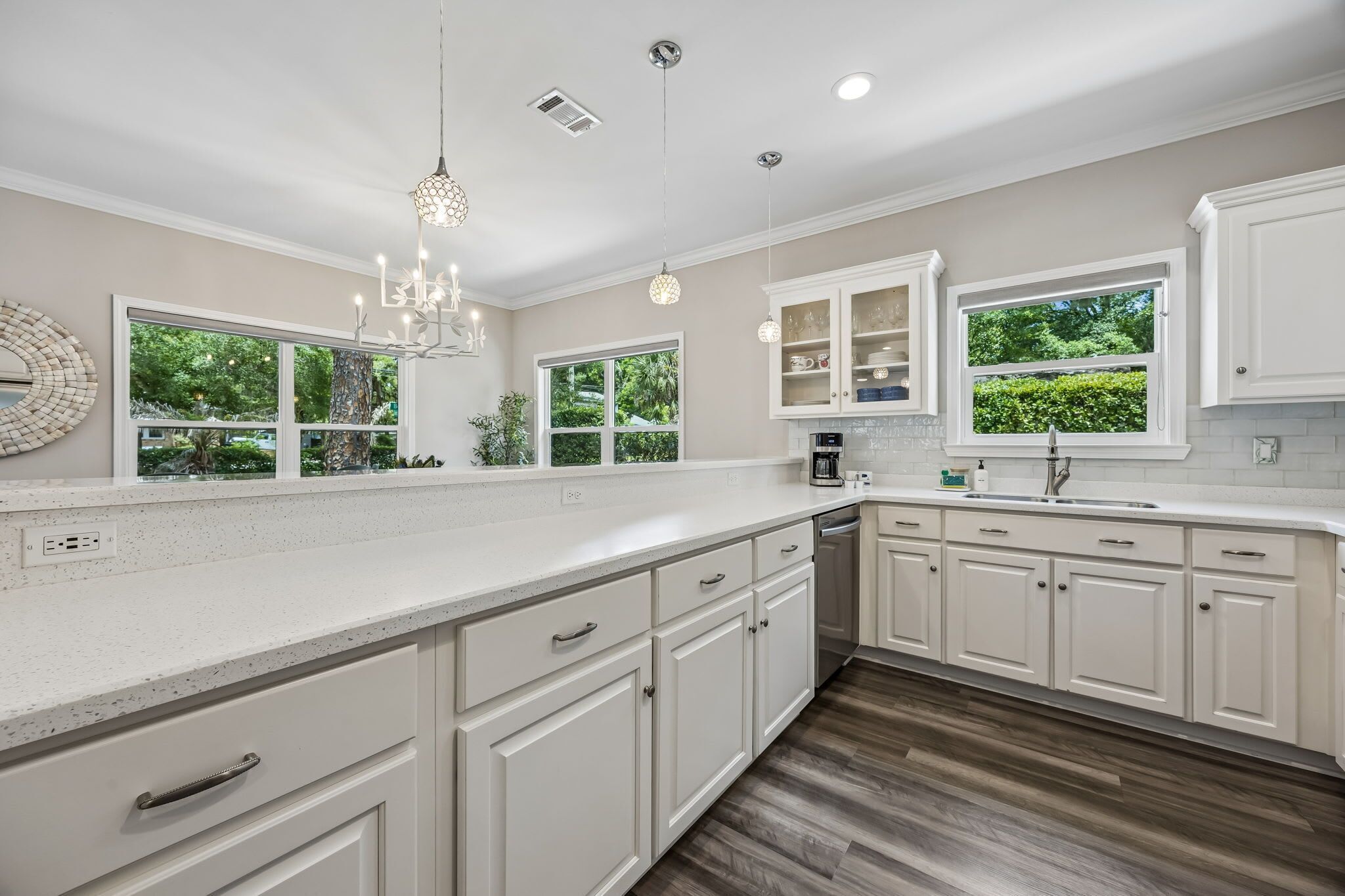 A modern kitchen with white cabinetry, a large island, and multiple windows offering views of greenery.