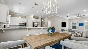 Une cuisine moderne avec des meubles blancs, des appareils en acier inoxydable et une table à manger en bois, assortie de chaises rembourrées.