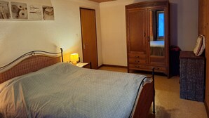 Un dormitorio con cama, armario de madera, mesita de noche con lámpara y aplique en la pared.