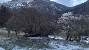 Un paisaje montañoso con picos nevados, un valle con vegetación escasa y un pequeño poblado con edificios tradicionales.