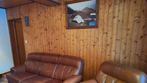 Una habitación con un sofá y un sillón de cuero marrón, paredes con paneles de madera y un cuadro en la pared.