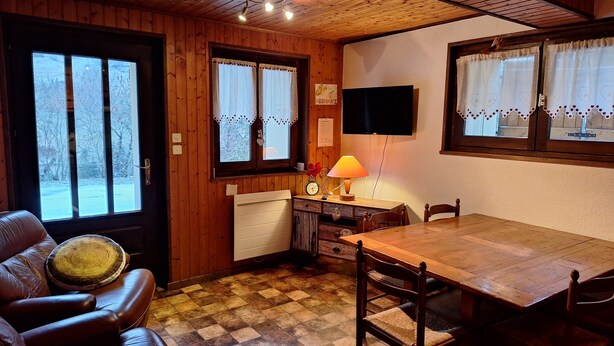Un interior de madera con suelo a cuadros, una mesa de comedor, sillas, un sofá y un televisor montado en la pared.