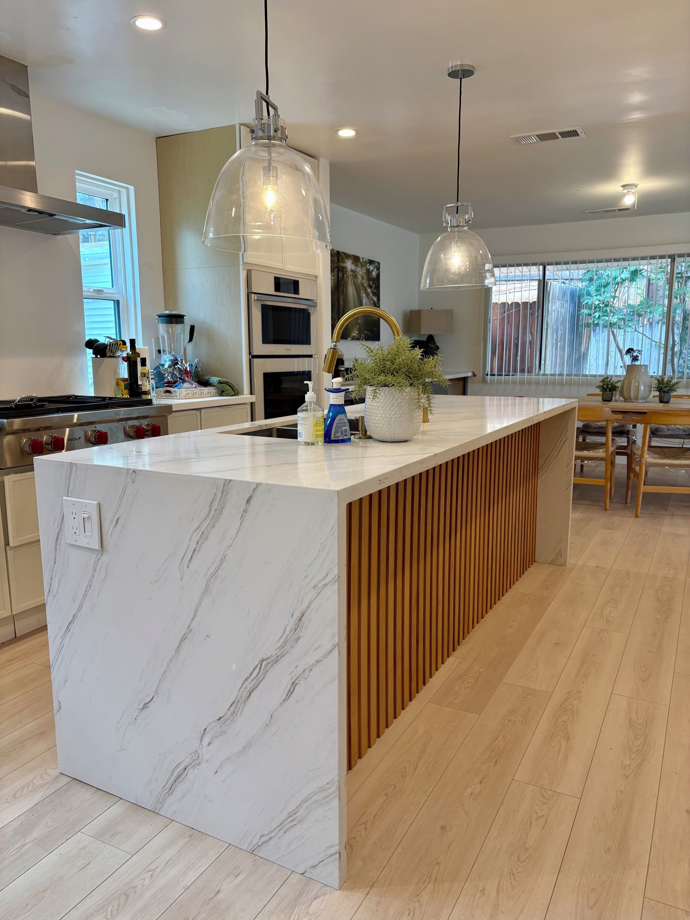 Una cocina moderna con encimeras de mármol, paneles de madera, luces colgantes y horno empotrado.