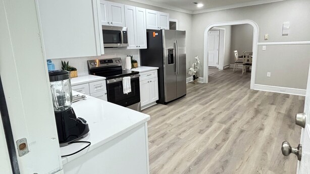 Una cocina moderna con armarios blancos, electrodomésticos de acero inoxidable y suelo de madera.