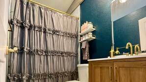 Een badkamer met douchegordijn, toilet, wastafel met spiegel en een wasbak.
