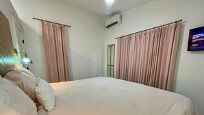 Een slaapkamer met een bed, gordijnen, een airconditioningapparaat, een televisie en een wandlamp.