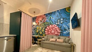 Een knus woongedeelte met een kitchenette, een bank, een eethoek en een kleurrijke bloemenmuur.