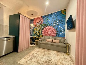 A compact living space with a kitchenette, a sofa, a dining area, and a vibrant floral mural on the wall.