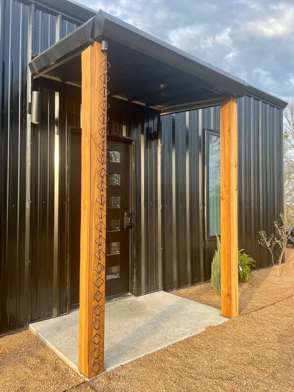 A modern building with a metal exterior, a wooden door, and a concrete entrance area.