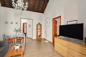 Ein Wohnzimmer mit Essbereich, einer Kristallleuchtre, einem Flachbildfernseher und einer Holzkommode.