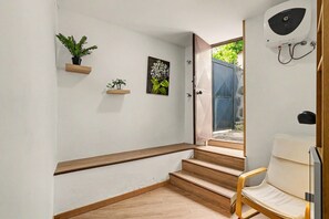 Un escalier avec des marches en bois menant à une porte, une chaise et deux étagères fixées au mur, sur lesquelles sont posées des plantes.