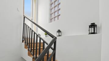Una escalera con barandillas negras y detalles de madera, que conduce a una plataforma con una planta en maceta y un farol negro.