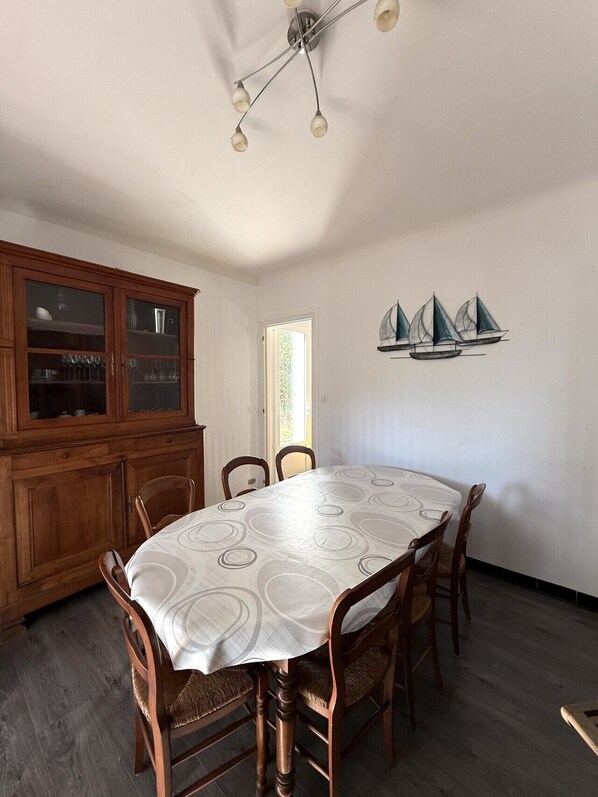 A dining area with a round table, wooden chairs, a wooden cabinet, and a wall-mounted sailboat decoration.