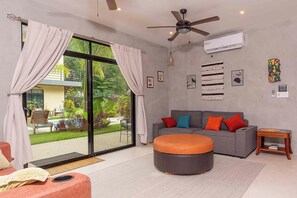 A modern living room with a grey sofa, orange ottoman, and a ceiling fan. - 2BR/2BA Retreat pool parking rancho, Walk to Beach (Playa Grande)