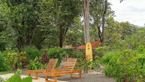 Ein Garten mit Holzliegen, einer gelben Struktur und verschiedenen Pflanzen.