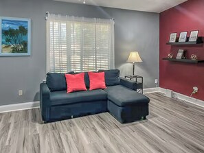 Una sala de estar con un sofá modular, una lámpara, un cuadro y una pared de acento roja.