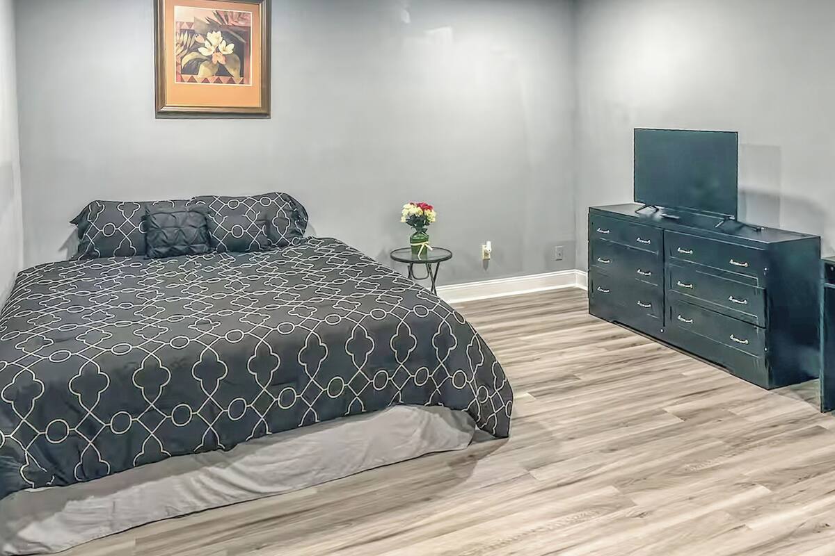 Un dormitorio con una cama, un aparador, un televisor y un cuadro en la pared.