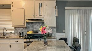 Uma cozinha com ilha central, banquetas de bar e um vaso de flores.