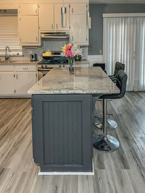 A kitchen with a central island, bar stools, and a vase of flowers.
