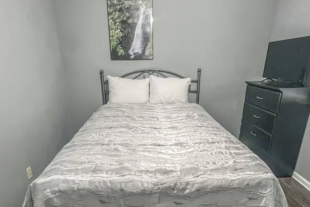 Una cama con una colcha estampada, un cabecero y un aparador oscuro con cajones.