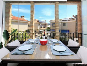 A dining table set with plates, cutlery, and wine glasses, with a view of buildings through large windows. - Alcazar by Interhome (Almuñécar)