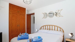 Une chambre à coucher comprenant un lit, une armoire en bois, des miroirs fixés au mur et une table de chevet avec une lampe.