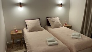 Una habitación de hotel con dos camas, una mesita de noche con lámpara y un aplique de pared.