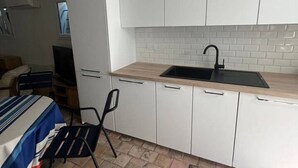 Una cocina compacta con armarios blancos, un lavamanos negro y un respaldo de azulejos.