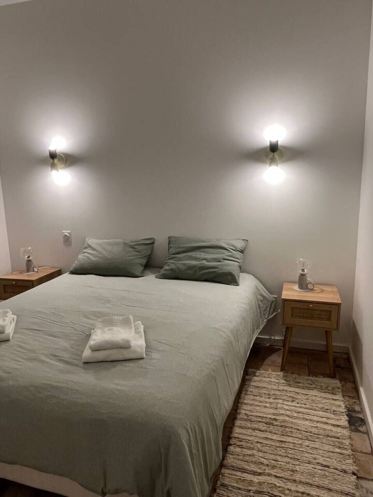 Ein ordentlich bezogenes Bett mit einer hellen Bettdecke, zwei Nachttische mit Lampen und ein gemusterter Teppich auf dem Boden.