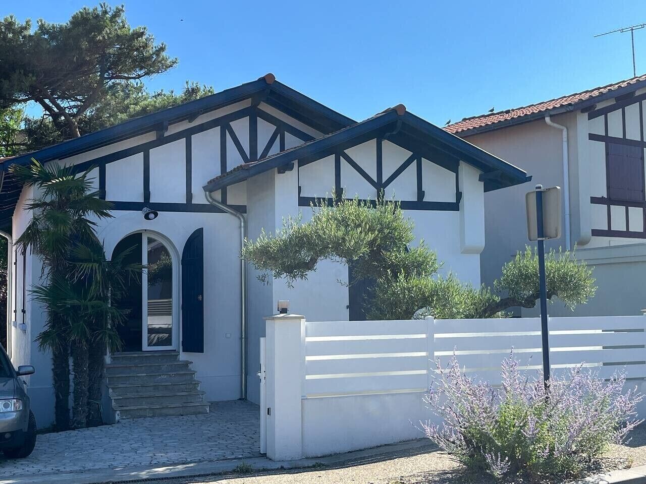 Ein zweistöckiges Haus mit weißer Fassade, dunklen Verzierungen und einer kleinen Veranda.