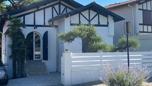 Una casa de dos pisos con fachada blanca, detalles oscuros y un pequeño porche delantero.