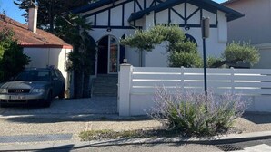 Una casa de dos pisos con fachada blanca, detalles oscuros y un porche cubierto.