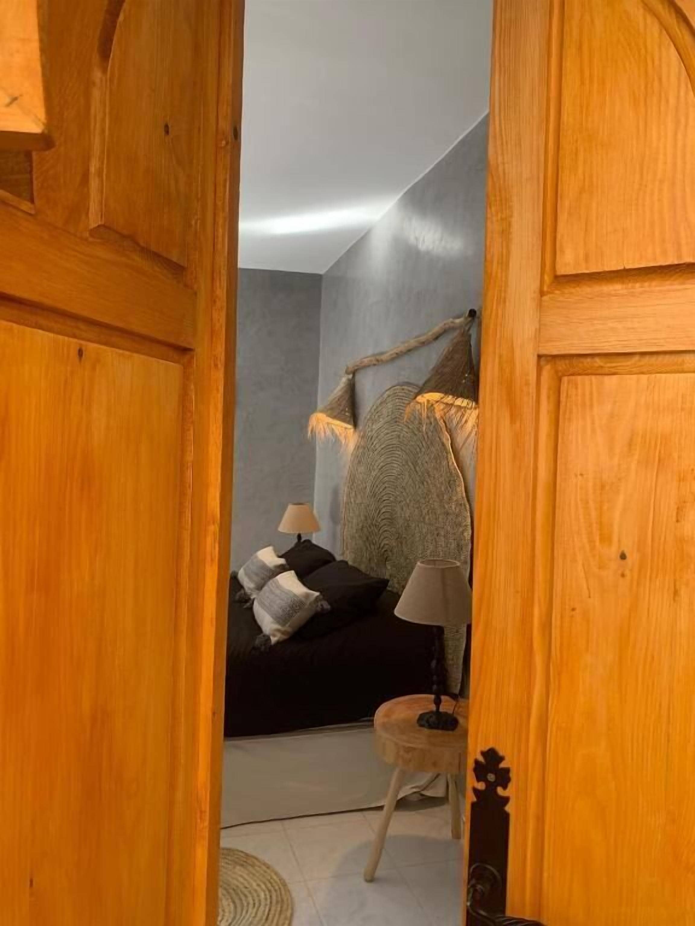 Un'apertura stretta che dà su una stanza con un letto, una lampada e un piccolo tavolo rotondo.