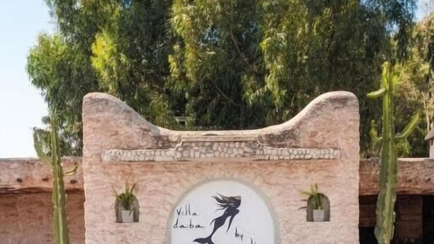 A pool with a stone wall and a circular sign with a silhouette of a woman and text. - Villa Daba by Zelia en Exclusivité  (Essaouira)