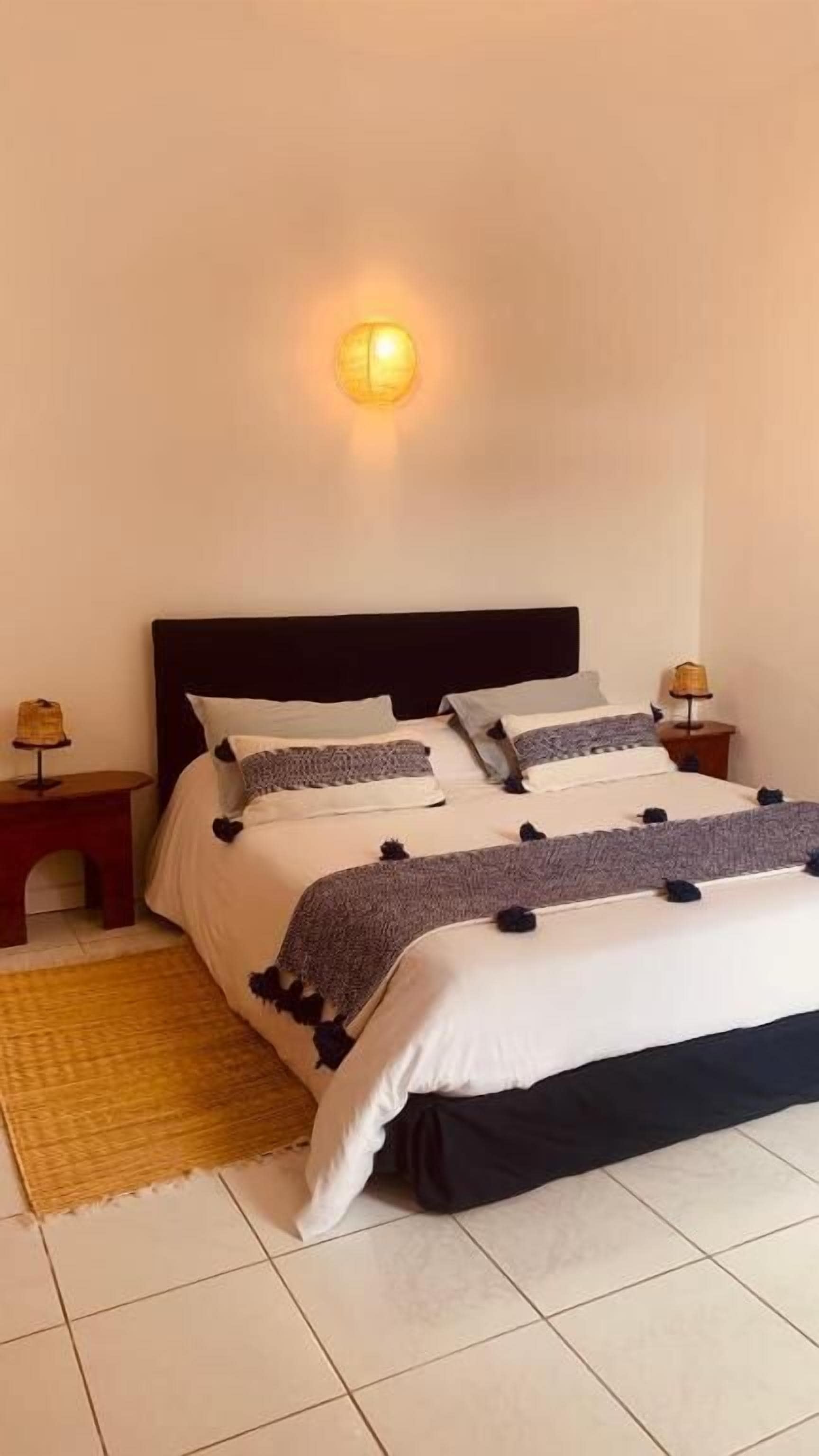 A neatly made bed with a black headboard, two bedside tables with lamps, and a wall-mounted light fixture.