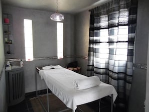 Een kamer met een enkel bed, een radiator, een plank met toiletartikelen en een raam met gordijnen.