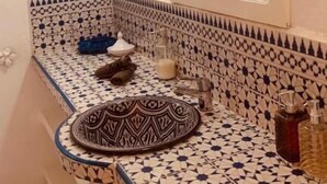 A bathroom with a patterned tile backsplash, a round sink with a decorative plate, a mirror, and a wall-mounted light fixture. - Villa Daba by Zelia en Exclusivité  (Essaouira)