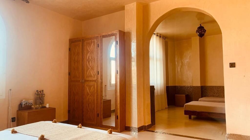 Un dormitorio con cama, armario y baño visible a través de un arco.